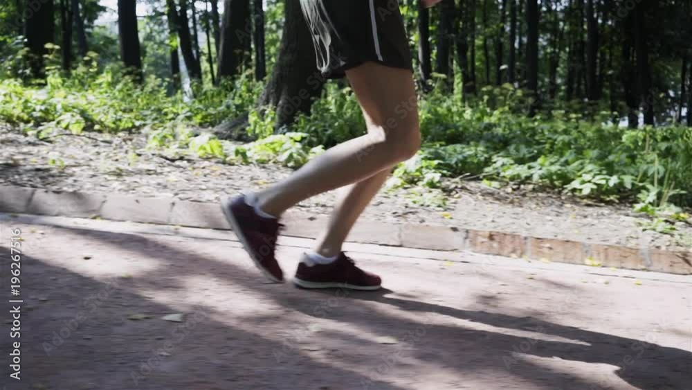 Side view of legs of an unrecognizable young woman jogging downhill in a park on a summer day. Tracking slow motion close up shot Side view of legs of an unrecognizable young woman jogging downhill in a park on a summer day. Tracking slow motion close up shot