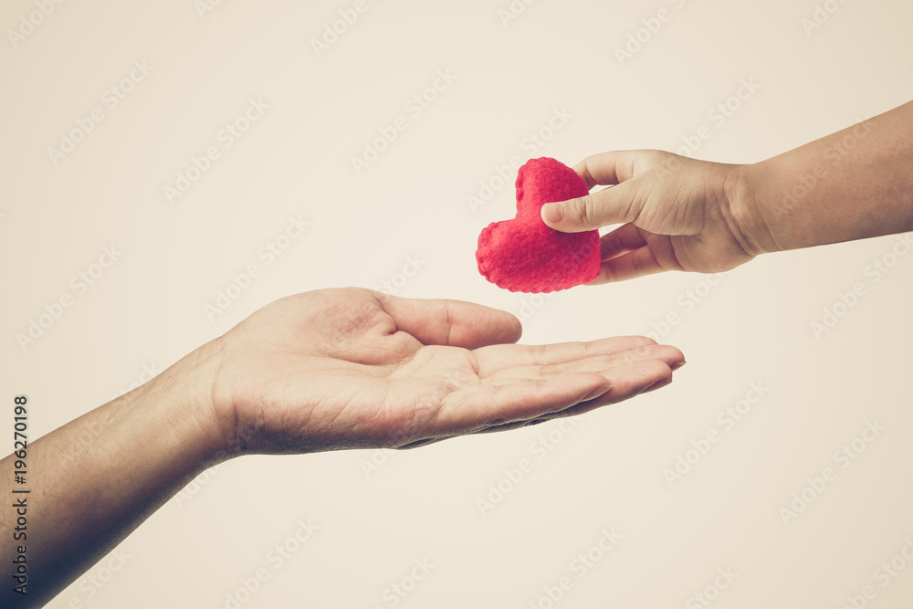 Baby's hand giving a red heart to mother's hand / Love and care between kid and mom / Mother's day concept