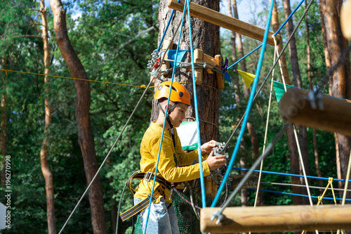 Happy child, healthy teenager school boy enjoys activity in a climbing adventure rope park on a sunny summer day