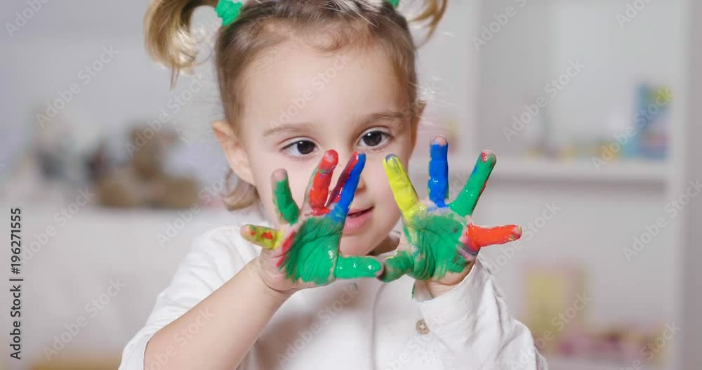 Portrait of a little girl in her bedroom showing her hands all colored with paint. Concept of: color, creativity, art, happiness and educational.