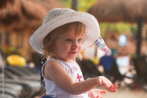 Portrait of Cute Adorable Two Years Old Toddler Girl with Blonde Hair and Big Blue Eyes in Summer White Hat is Sending Air Kiss,sitting at the Pool Area in Cancun Resort in Mexico, March 2018