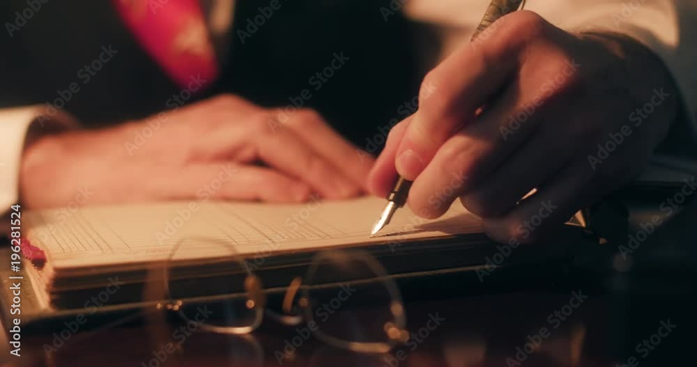 1940s period piece of businessman hands using a classic fountain pen to make entries into a company ledger. 1940s period piece of businessman hands using a classic fountain pen to make entries into a company ledger.