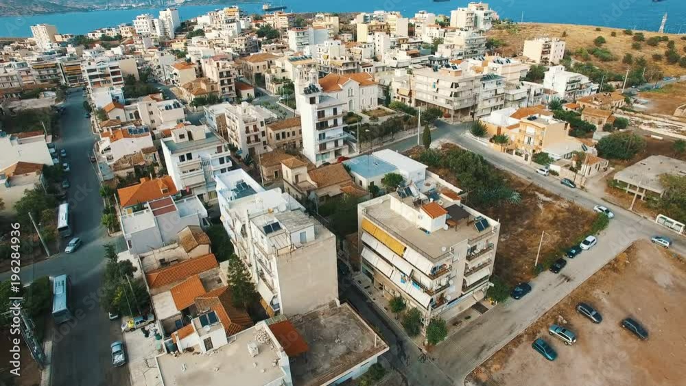 Flying over buildings of small town in southern Europe at sunset. Low-rise buildings, flat roofs, narrow streets, small cars, public squares, gardens. Aegean sea. Lavrio town, Attica, Greece. Aerial. Flying over buildings of small town in southern Europe at sunset. Low-rise buildings, flat roofs, narrow streets, small cars, public squares, gardens. Aegean sea. Lavrio town, Attica, Greece. Aerial.