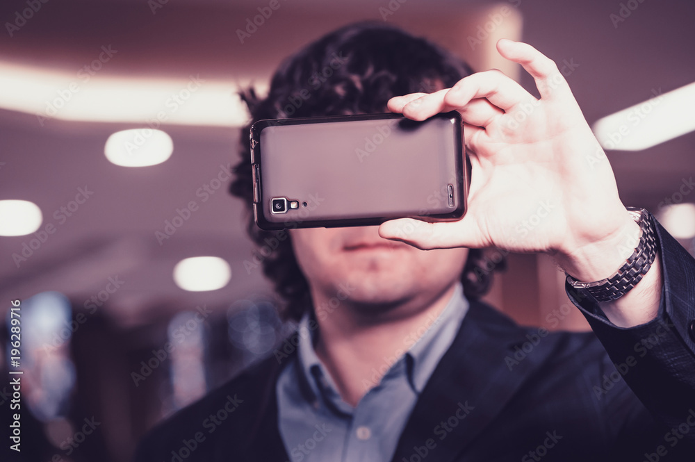 Business man looking at smartphone screen. Guy hides behind the mobile phone. Magenta tone