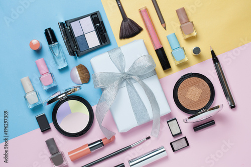 Beauty, decorative cosmetics and gift box with bow. Makeup brushes set and color eyeshadow palette on bright multicolor and blue background , flat lay, top view, Minimalistic style.