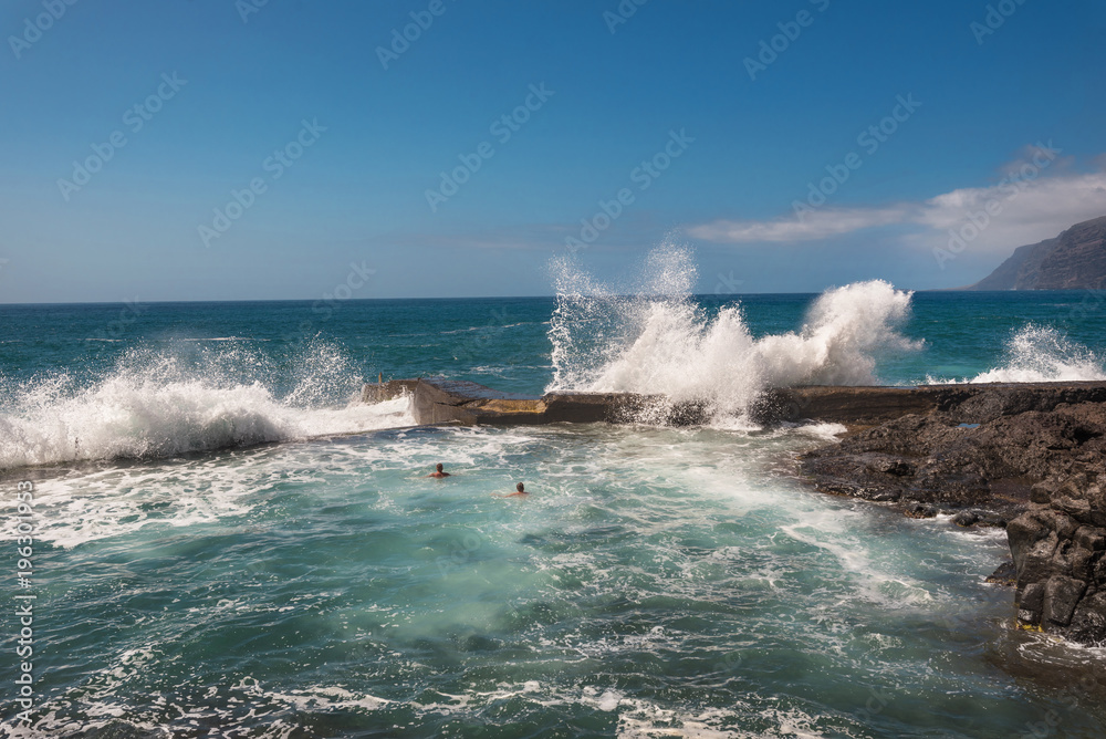 Unidentifiable Tourist swimming in coastline landscape in Puerto Santiago, Tenerife, Spain.