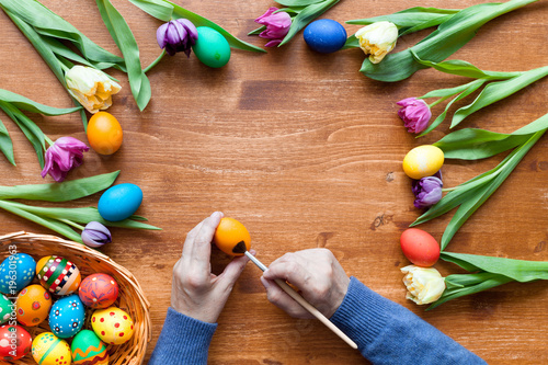 Woman paints easter eggs, wood easter background, top view