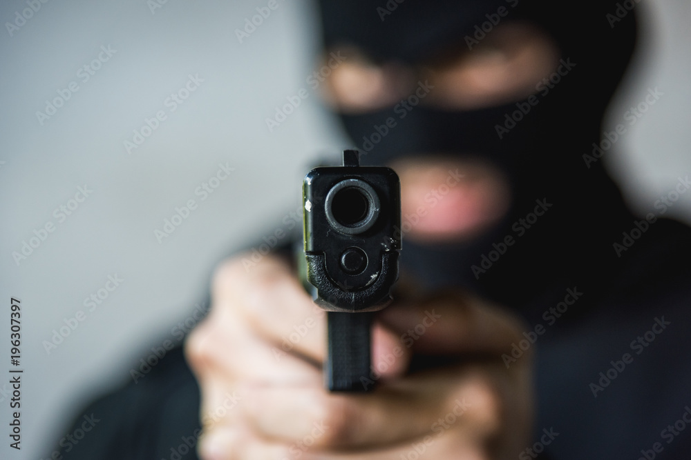 Masked robber with hand gun pointing aiming Masked robber with hand gun pointing aiming