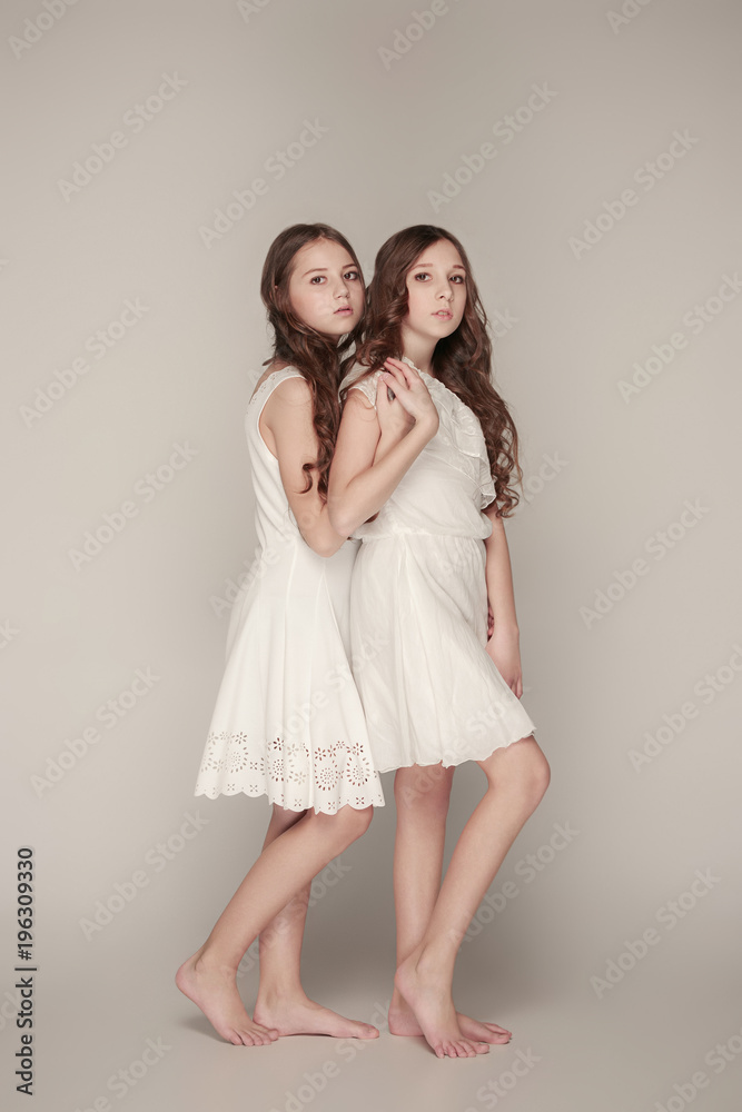 The fashion girls standing together and looking at camera over gray studio background The fashion girls standing together and looking at camera over gray studio background