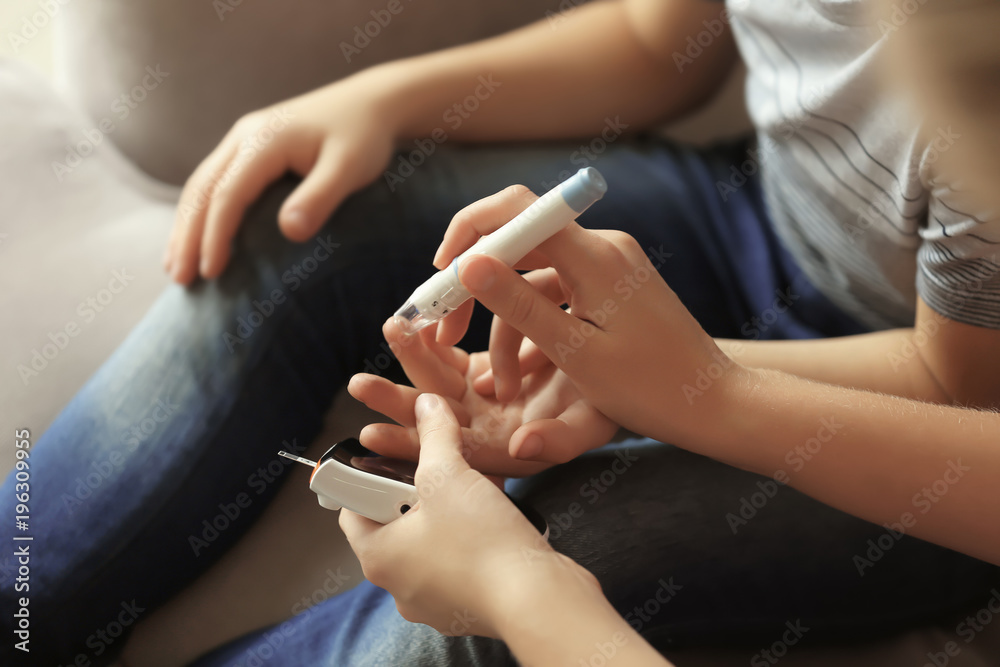 Woman and her diabetic son with lancet pen and digital glucometer taking blood sample at home, closeup