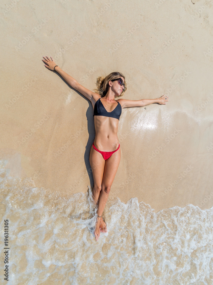 Fototapeta premium Top view of a woman at the tropical beach relaxing on the sand