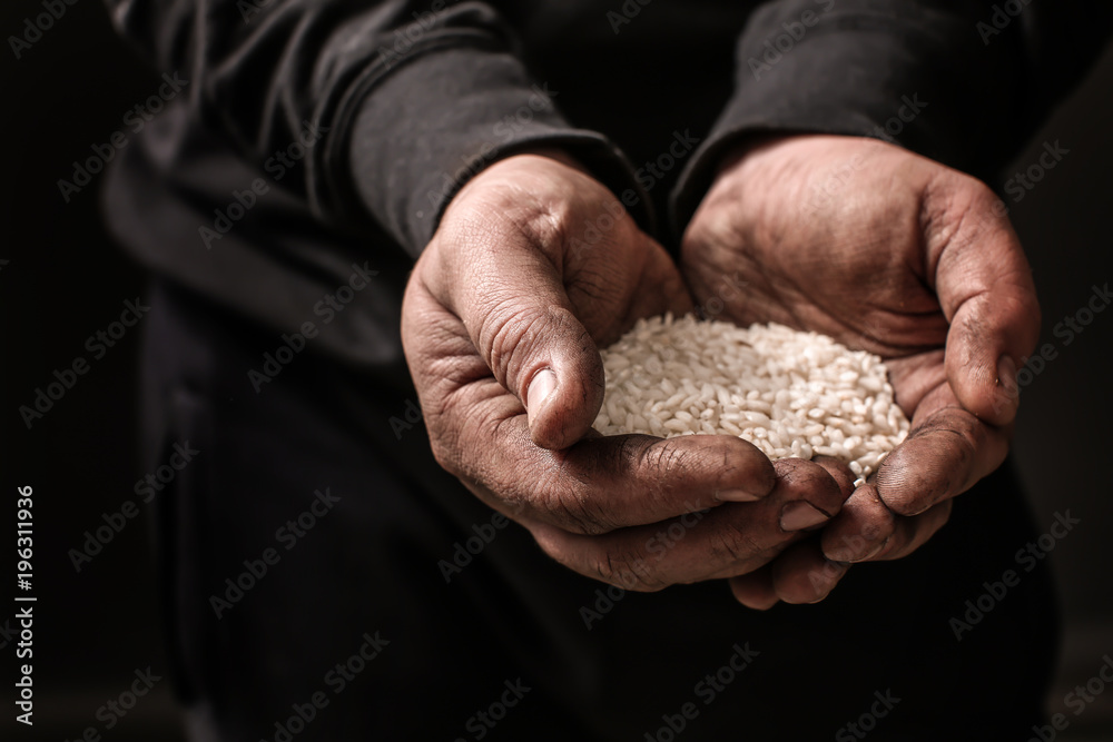 Poor man holding rice in hands on dark background Poor man holding rice in hands on dark background