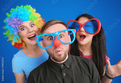 Young people in funny disguise posing on color background. April fool's day celebration