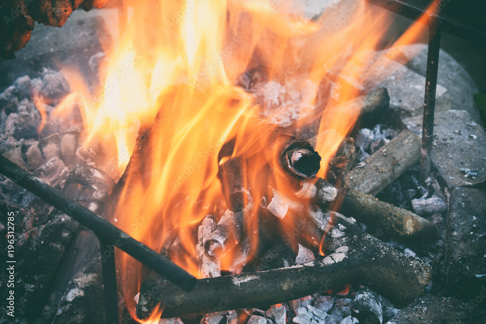 Fototapeta premium Burning firewood in the bonfire. Flames burning in the grill with smoke. Arson or natural disaster. Texture of fire and flame, dark background