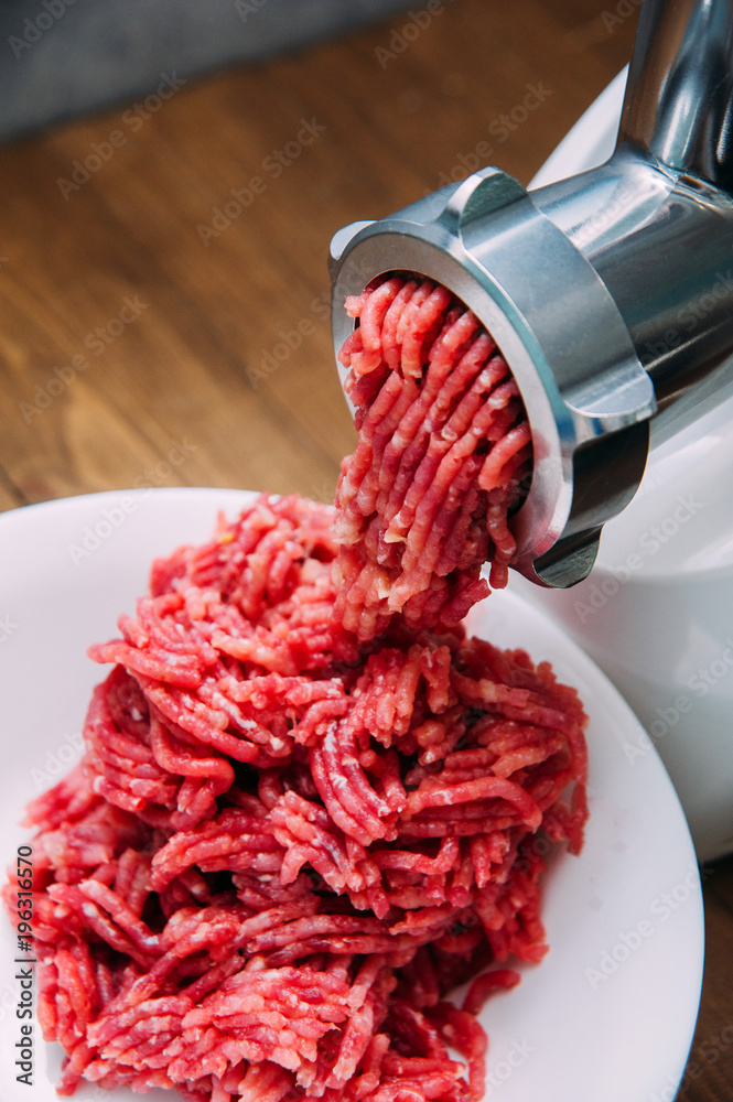 Meat grinder in action and ground beef meat. electric meat grinder.  Unidentifiable butcher holding tray full of minced raw red meat leaving  machine in Stock Photo - Alamy