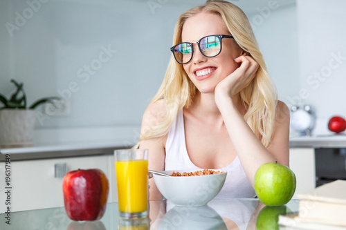 beautiful smiling young woman in eyeglasses eating breakfast at home