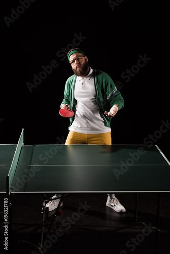 bearded sportsman with tennis equipment standing at table isolated on black