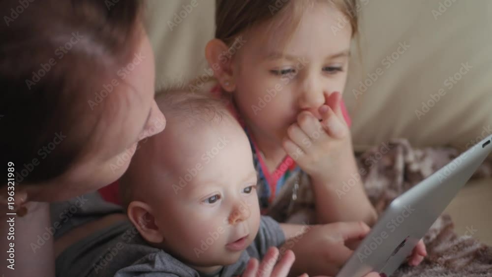 Mother and children with a tablet computer at home watching cartoons and playing. Mother and children with a tablet computer at home watching cartoons and playing.