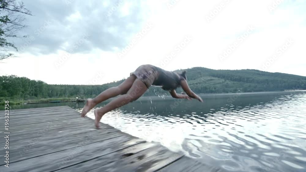 Side view of plump black woman running on wooden dock, speeding up and jumping into water with big splashes, rear view