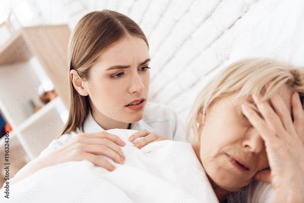 Girl is nursing elderly woman at home. Woman is feeling bad, girl is concerned. Girl is nursing elderly woman at home. Woman is feeling bad, girl is concerned.
