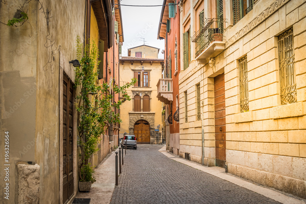 Typical European small narrow cobblestone street with beautiful bright houses, windows with shutters. Bright sunny summer day in Italy, Verona