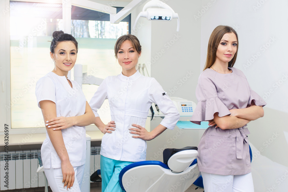 Obraz premium Cheerful group of young dentists and their assistants standing in the dental office and looking at camera and friendly smiling at white background of medical room.