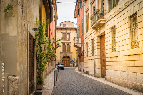 Typical European small narrow cobblestone street with beautiful bright houses  windows with shutters. Bright sunny summer day in Italy  Verona
