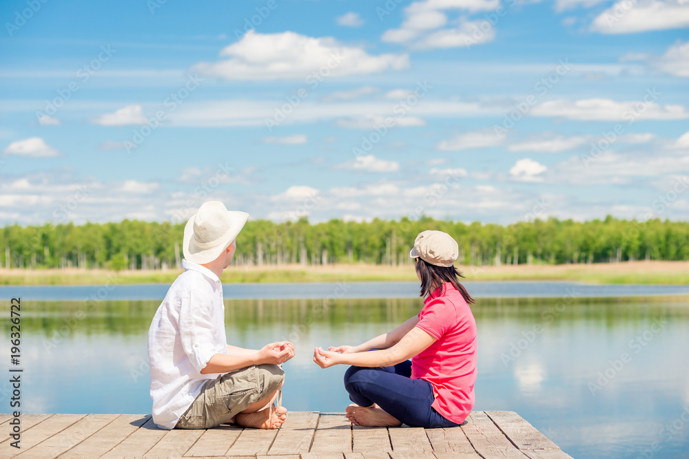 Fototapeta premium couple in love relax in a lotus pose on a wooden pier near the lake