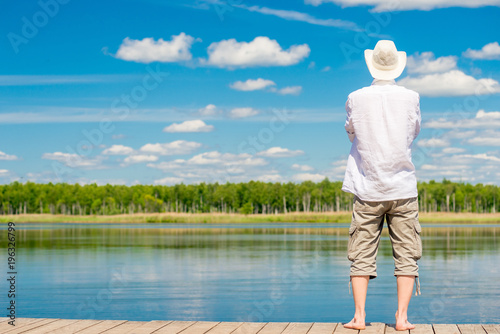 view of a piny pine young man with bare feet stands on a wooden pirsen against a beautiful lake