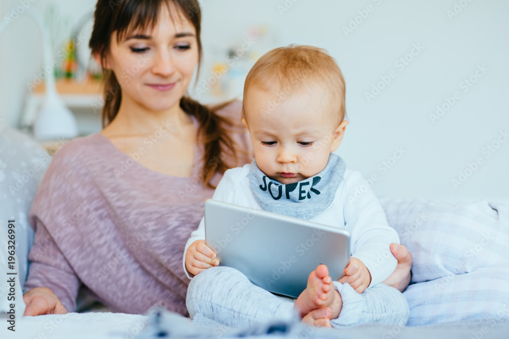 Family shoot portrait of european woman and infant baby concentrated looking in tablet together at cozy home interior. Family shoot portrait of european woman and infant baby concentrated looking in tablet together at cozy home interior.