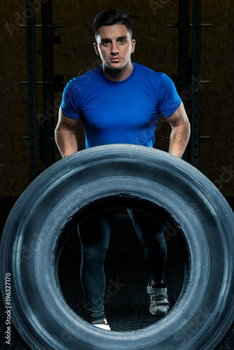 portrait of a strong athlete with a large heavy wheel in the gym