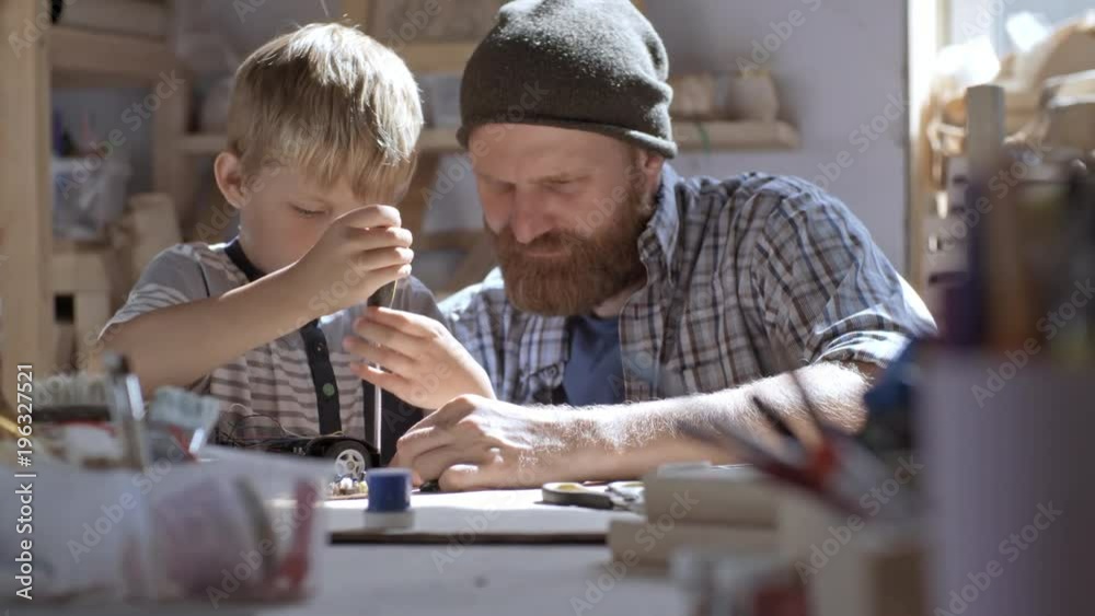 Boy of primary school age using screwdriver to drive screws into deconstructed toy car when repairing it with his father Boy of primary school age using screwdriver to drive screws into deconstructed toy car when repairing it with his father