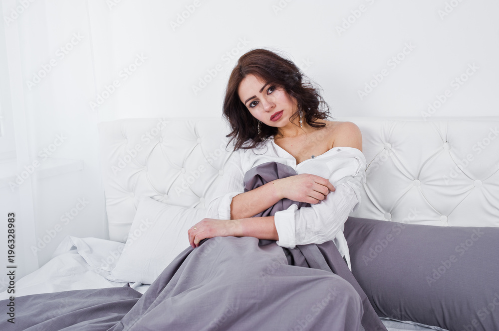 Studio portrait of brunette girl in white blouse lying on bed. Studio portrait of brunette girl in white blouse lying on bed.