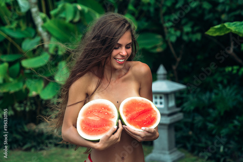 Portrait beautiful brunette girl in swimsuit with watermelon fruit holding in hands. Sexy model with perfect body, cute smile posing. Concept of sport, vegetarian and healthy food