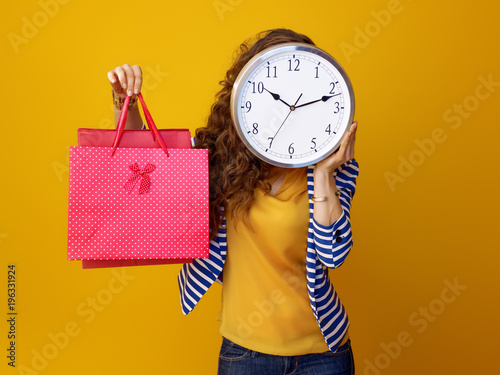woman holding clock in front of face and showing shopping bags