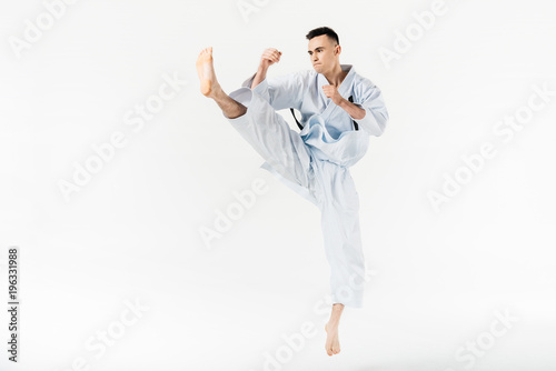 Male karate fighter performing kick isolated on white