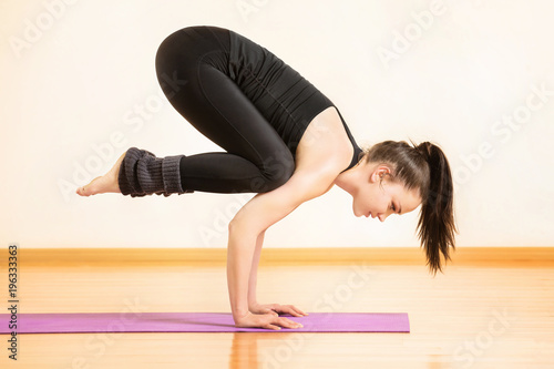 Young woman is practising yoga in bhujapidasana pose at gym background. photo