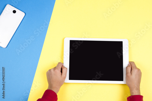 Kid hands holding tablet computer on blue and yellow background