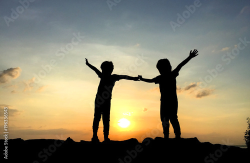 Silhouette of two sibling playing together at the beach on sunset 