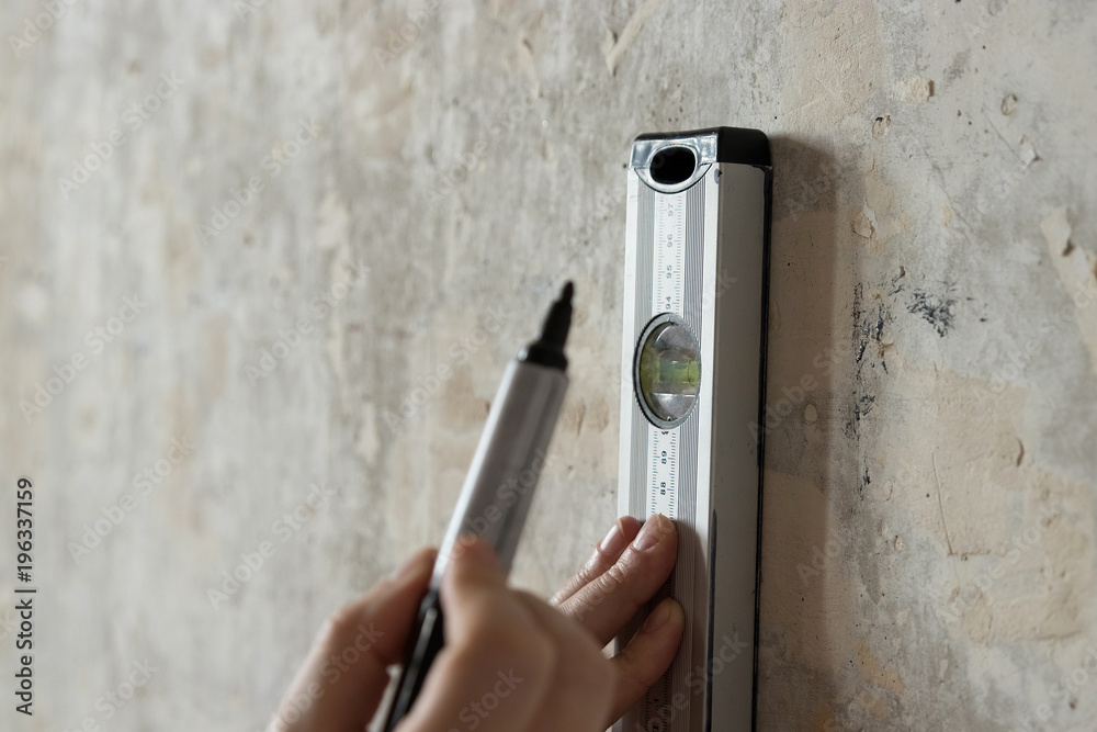 A man measures on the wall with a ruler, a tape measure, a level, marks ...