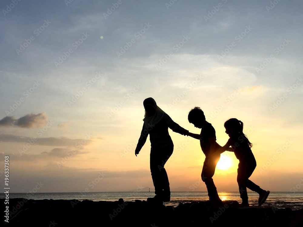 Silhouette of young mother and sibling playing together at the beach on sunset	