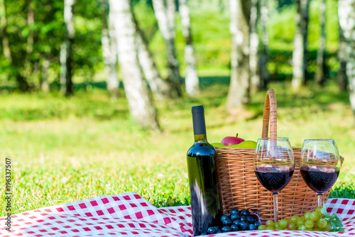 red wine and ripe grapes lie on a tablecloth on a lawn oklo basket for a picnic