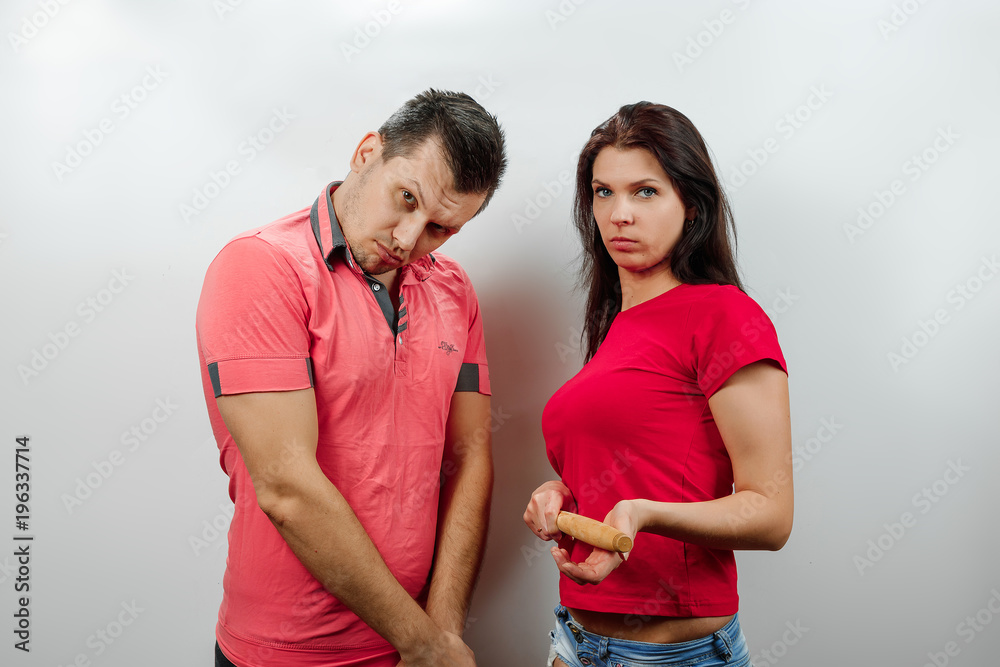 Fototapeta premium Family quarrel, wife scolds her husband, young, beautiful wife beats her husband with a stick. The concept of the psychology of family relations, marriage, domestic conflicts, domestic violence.