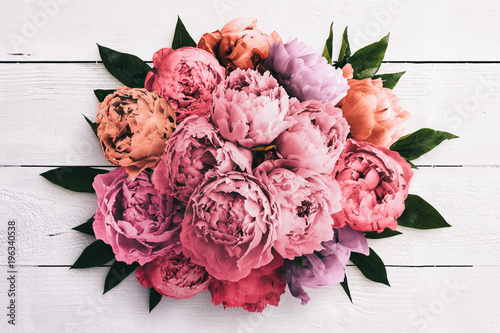 Fotografi A peony centerpiece flower arrangement with different colors and leaves on a white wood background