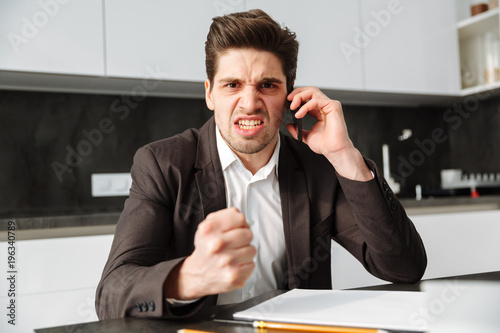 Angry young businessman talking by mobile phone.