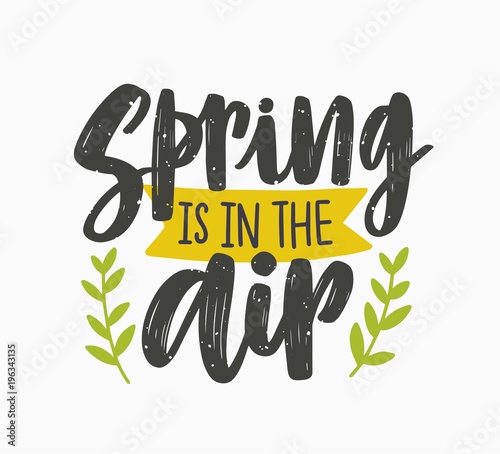 Spring Is In The Air inspiring phrase written with artistic cursive font or script and decorated with green leaves or branches. Seasonal lettering isolated on white background. Vector illustration.