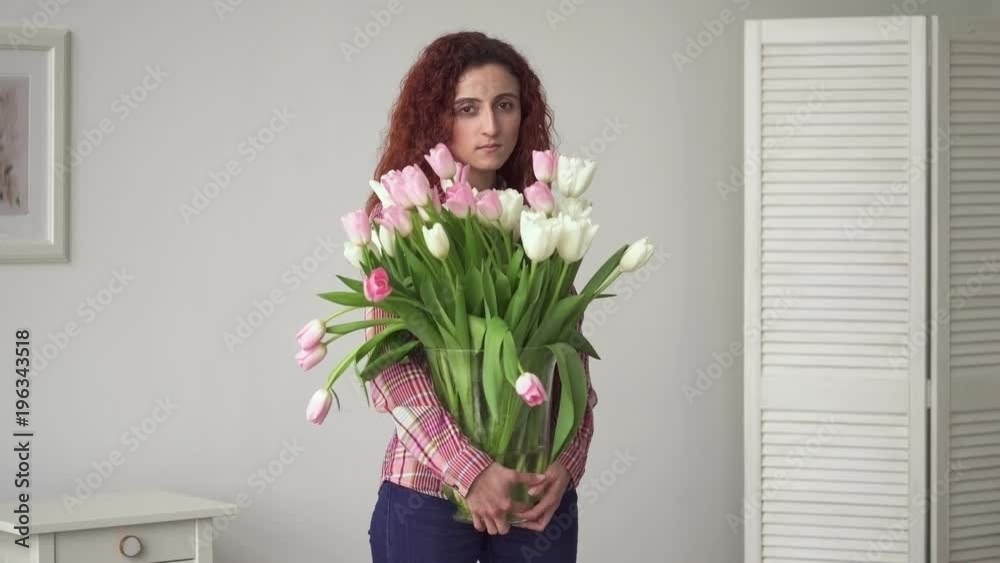 Young middle eastern woman with sad eyes holding flowers in hands at home Young middle eastern woman with sad eyes holding flowers in hands at home