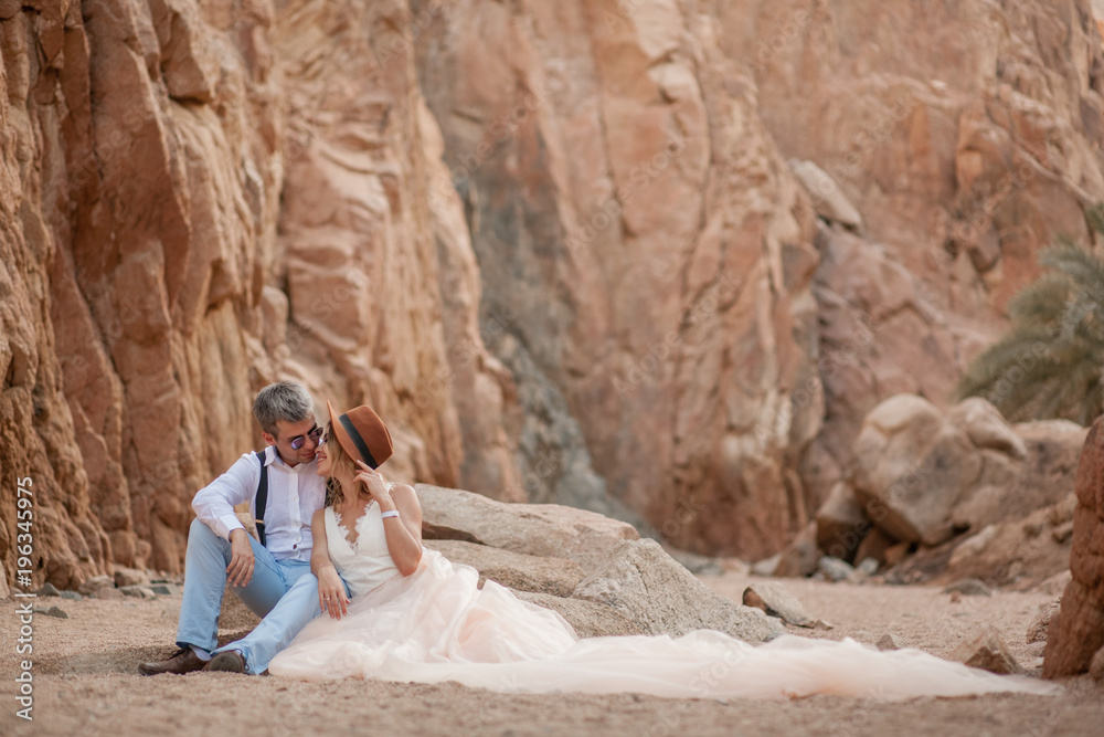 Bride and groom sit and smile in canyon on background of rocks.