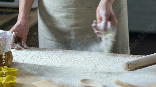 Hands of female cooker preparing working place and sprinking flour on table photo