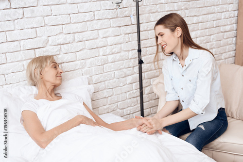 Girl is caring for elderly woman at home. They are holding hands.